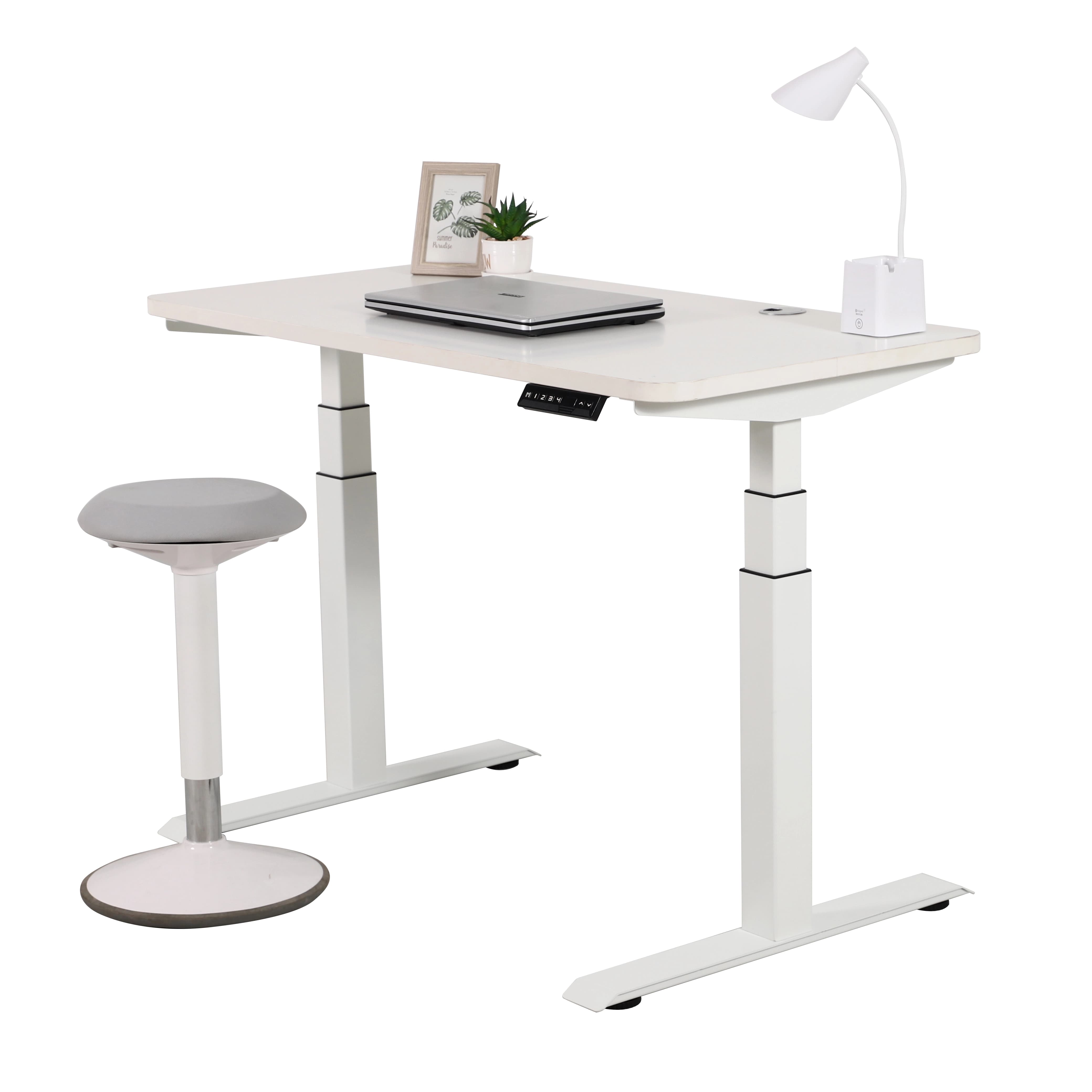 Un escritorio de pie ajustable 2B3 blanco con tablero blanco, equipado con una computadora port&aacute;til, una planta peque&ntilde;a y una l&aacute;mpara de escritorio. Junto al escritorio hay un taburete ergon&oacute;mico gris y blanco, todo ello sobre un fondo blanco.